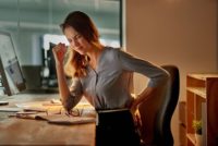 Businesswoman holding her back in pain while working at her desk