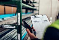 Female warehouse clerk using phone and looking at purchase order